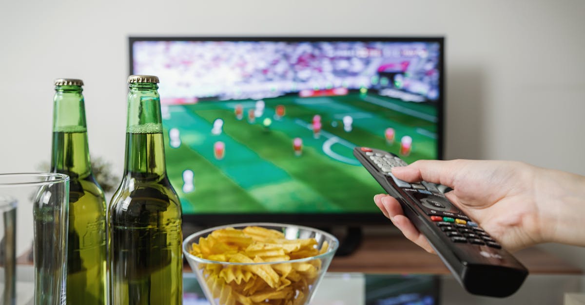 A person holding a remote while watching soccer on TV with beer and snacks on the table. - The Global Phenomenon: 15 Reasons Why the World Stops for the World Cup