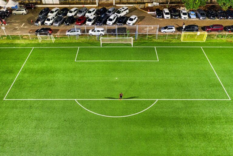World Cup controversies - Aerial view of a soccer field at night in Jakarta with a lone player casting a shadow under stadium lights.