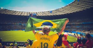 Excited Brazilian fans holding flag at soccer match in vibrant stadium atmosphere. Winning Streaks in World Cup. World Cup Victories